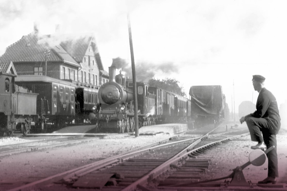 Historisk bild på järnvägsstationen i Klippan. I föregrunden ses en stins som lägger om en växel. Foto.