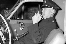 Historisk bild på en polis som sitter i sin bil och pratar i kommunikationsradion. Foto.