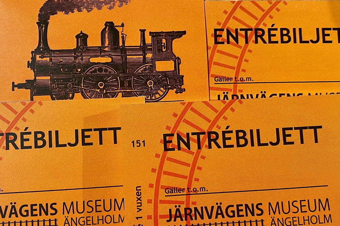Fyra entrébiljetter till museet. Orange bakgrund med svart text och logotype. Foto.